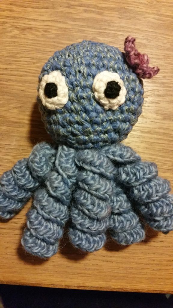 A Crocheted Amigurumi Octopus with Flower on a table